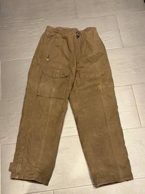 Bruna vintage Fjällräven cargobyxor med fickor - Snygga bruna vintage Fjällräven cargobyxor med stora benfickor och justerbara benslut med kardborre. Byxorna har resår i midjan och dragkedja fram. Perfekta för en avslappnad streetstil och praktiska med flera fickor. Materialet känns slitstarkt och passar till många outfits. Nypris 3000-4000kr,  Storlek M. Säljer de för 1500kr, pris kan diskuteras.