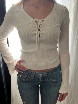 Vit ribbad långärmad topp med snörning - Trendig vit ribbad topp med lång ärm och snygg snörning framtill. Toppen har en v-ringad halsringning.💕
