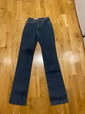 Marlboro Classics raka jeans blå stl 26 - Säljer ett par raka blå jeans från Marlboro Classics med klassisk femficksdesign och normalhög midja. Jeansen har bälteshällor och stängs med knapp och dragkedja. Perfekta för dig som gillar en tidlös och avslappnad look.