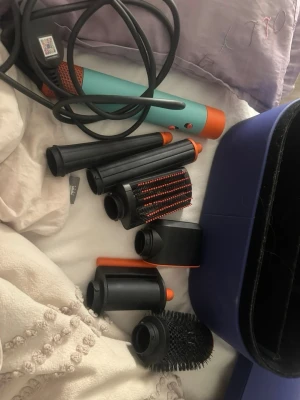 Dyson Airwrap multistyler med tillbehör - Säljer en Dyson Airwrap multistyler i turkos och orange med flera olika stylingtillbehör som borstar och locktillbehör. Perfekt för att skapa olika frisyrer och volym. Kommer med en snygg blå förvaringsbox.