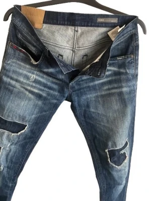 Blå slitna jeans från Dondup - Säljer ett par blå jeans från Dondup  med snygga slitningar . Jeansen har klassisk femficksdesign, normal midja och är tillverkade i denim. Perfekta för en avslappnad och trendig look. Jeansen är väldigt sällsynta och perfekt passform