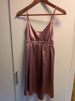 Rosa satinklänning med smala axelband - Supersnygg rosa satinklänning från Gina Tricot med smala axelband och v-ringning. Klänningen har markerad midja med resår och ett glansigt material som ger en lyxig känsla. Perfekt för dig som vill sticka ut med en trendig look.