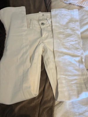 Vita raka jeans med fickdetaljer - Säljer ett par vita jeans med raka ben och snygga fickor med lock och knapp bak. Jeansen har hällor för skärp och klassisk knappgylf. Perfekta för en clean och fräsch look. Materialet är denim i bomull.
