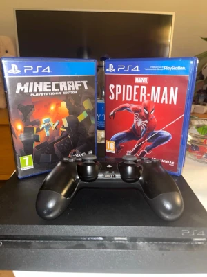 PlayStation 4 med handkontroll och spel - Säljer en svart PlayStation 4 med en svart DualShock 4-handkontroll. Två spel ingår: Minecraft och Marvel's Spider-Man, båda i originalfodral. Konsolen har en stilren, rektangulär design i plast och passar perfekt för gamingkvällar.