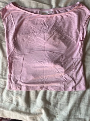 Ljusrosa croppad topp med knyt - Säljer en ljusrosa croppad topp i mjuk bomull. Toppen har en öppen rygg med breda knytband som ger en snygg detalj. Perfekt för dig som gillar en enkel men trendig stil.