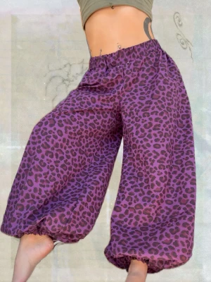 Lila leopardmönstrade byxor Funky Fig - Unika lila byxor med svart leopardmönster från Funky Fig. Vida ben och resår i midja och benslut ger en avslappnad och cool siluett. Perfekta för dig som vill sticka ut med ett djurmönstrat statement-plagg. Sytt av bomullsväv! Passar S-L- jag är storlek M. 
