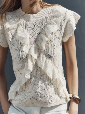 Beige stickad blus med volang - Supersöt beige stickad blus med korta ärmar och volangdetaljer framtill. Blusen har ett vackert spetsmönster och rund halsringning. Perfekt för dig som gillar romantisk och feminin stil.