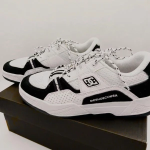 Svarta och vita sneakers från DC Shoes - Snygga sneakers från DC Shoes i svart och vitt med klassisk logga på sidan. Skorna har snörning och perforerade detaljer för extra stil. Perfekta för dig som gillar streetwear och vill ha en sportig look.