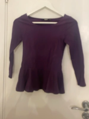 Lila topp med volang från BikBok - Snygg lila topp från BikBok med trekvarts ärm och volang nertill. Modellen har en feminin passform och är perfekt att styla med jeans eller kjol. Toppens material känns mjukt och stretchigt, vilket gör den bekväm att bära hela dagen.