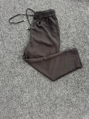 Svarta mjukisbyxor med dragsko från Zara - Säljer ett par svarta mjukisbyxor från Zara med elastisk midja och dragsko. Byxorna har raka ben och är tillverkade i ett mjukt och bekvämt material, perfekta för en avslappnad stil. Passar dig som gillar enkel och stilren design.