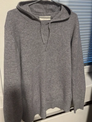 Grå cashmere hoodie från Sayless - Mjuk och stilren grå stickad hoodie från Sayless i lyxig cashmere. Tröjan har långa ärmar och huva. Perfekt för dig som gillar en enkel men exklusiv look.