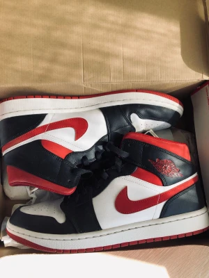 Nike Air Jordan 1 High svart/röd/vit - Säljer ett par Nike Air Jordan 1 High sneakers i svart, rött och vitt läder. Klassisk siluett med röd swoosh, svart snörning och ikonisk Air Jordan-logga på sidan. Perfekta för dig som gillar streetwear och vill sticka ut med en tidlös modell.