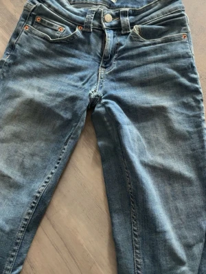 Blå jeans med fickdetaljer - Snygga blå jeans i klassisk tvätt med fem fickor och coola ficklock bak. Jeansen har låg midja, raka ben och detaljer i silverfärg. Perfekta för en avslappnad stil och passar till det mesta. Materialet är mjukt denim som känns bekvämt hela dagen.