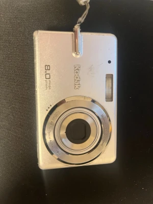 Kodak EasyShare M883 digitalkamera - Snygg silverfärgad digitalkamera från Kodak, modell EasyShare M883 med 8.0 megapixlar. Kameran har en kompakt rektangulär form, stor display på baksidan och inbyggd blixt. Tillverkad i metall och plast, perfekt för att fånga minnen med stil.    Saknar batteri och sim kort så kan ej testa den - ingen garanti på att den funkar