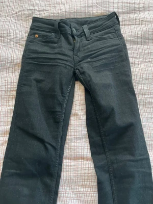 Svarta Cheap Monday jeans - Svarta jeans från Cheap Monday med klassisk femficksmodell och har en bootcut design. Jeansen har en rosa logga bak på linningen och är tillverkade i stretchigt denimtyg för en bekväm passform. Perfekta för en cool och avslappnad stil. Och har storlek 24 i midjan och 30 i längden 
