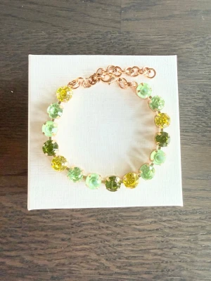 Armband med gröna/gula stenar  - Snyggt armband med 8 mm stora glittriga stenar i olika nyanser av grönt/gult, infattade i guldfärgad metall. Armbandet har justerbar kedja och ger en fräsch och trendig look. Perfekt accessoar för att lyfta din outfit. Sista bilden är ett urval av färger som finns. 