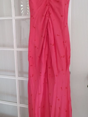 Rosa långklänning från Adoore - Supersnygg rosa långklänning från Adoore med små blommiga detaljer. Klänningen har en figurnära passform och är ärmlös, perfekt för sommarens alla tillfällen. Tunn och lätt i materialet, vilket gör den skön att bära varma dagar.