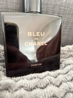 Bleu de Chanel Parfum - Säljer en exklusiv Bleu de Chanel Parfum. Flaskan är mörkblå och elegant med guldiga detaljer och klassisk Chanel-logga på korken. Parfymen kommer i en stilren, fyrkantig glasflaska som utstrålar lyx och modernitet.