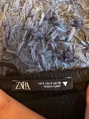 Svart kort klänning från Zara - Snygg svart kort klänning från Zara i storlek S. Klänningen har en strukturerad yta och är ärmlös med en lätt utställd kjol. Perfekt för dig som gillar en enkel men trendig look.