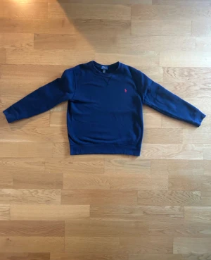 Marinblå sweatshirt från Polo Ralph Lauren - Klassisk marinblå sweatshirt från Polo Ralph Lauren. Tröjan har varit använd 3-5 gånger relativt ny. Storlek 160cm men jag är 170cm och passar bra  på mig. Varan bär en QR länk som bevisar att varan är äkta.