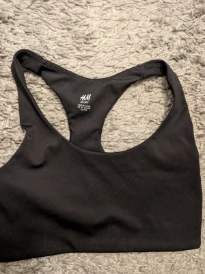 Svart sport-bh från H&M Sport stl xs - Säljer en svart sport-bh från H&M Sport i storlek XS. Bh:n har brottarrygg och är tillverkad i ett stretchigt, mjukt material som passar perfekt för träning och gym. Enkel och stilren design utan vaddering eller bygel.