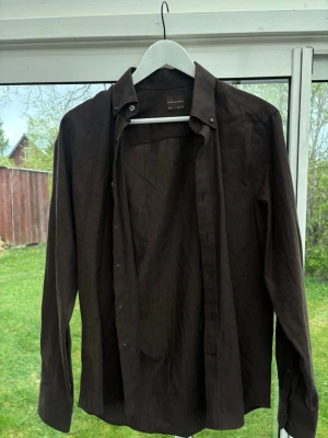 Mörkbrun linneskjorta Oscar Jacobson - Snygg mörkbrun skjorta från Oscar Jacobson i linnematerial. Skjortan har lång ärm, klassisk krage och knappar framtill. Perfekt för dig som gillar stilrena och tidlösa plagg med en relaxed vibe.