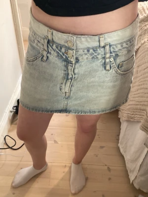 Ljusblå jeanskjol  - Trendig ljusblå jeanskjol i kort modell och klassiska femficksdetaljer. Kjolen har bälteshällor, knapp- och dragkedjestängning samt en cool patchdetalj baktill. Perfekt för dig som gillar en avslappnad och stilren denimlook.