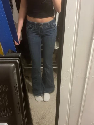 Blå bootcut jeans med detaljer - Blå jeans ifrån Nelly med detaljer på backfickorna. Dom är i storlek 32 och har använts ganska mycket men i bra skick. De ända är att en tråd har gått upp på ena backfickan som man ser på bild 3💞