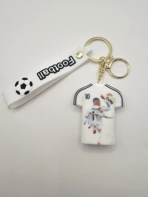 Nyckelring Mbappé fotbollströja - Säljer en vit nyckelring med fotbollstema, formad som en tröja med Mbappé och nummer 10. Nyckelringen har även ett vitt band med texten 'Football' och en fotbollsgrafik. Perfekt accessoar för fotbollsfans!