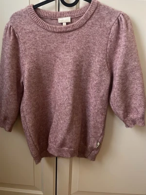 Ljuslila stickad tröja från pomp de lux - Supersöt ljuslila stickad tröja från PompDElux med puffärmar och rund halsringning. Tröjan har ribbade muddar vid fållen. Perfekt för dig som gillar en mjuk och trendig look. Passar som en xs. 