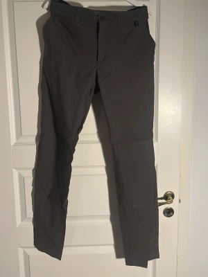 Mörka bruna chinos med rak passform, Peak Performance  - Snygga bruna chinos med rak passform och klassisk design. Byxorna har framfickor, bälteshällor och knappgylf. Materialet ser ut att vara lätt och bekvämt, perfekt för en clean och stilren look.