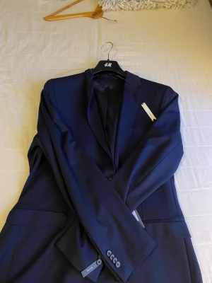 Mörkblå kostym från Blazers Jersey SF - Snygg mörkblå kostym från Blazers Jersey SF. Med klassisk kavaj Kavajen har två knappar framtill, fickor med lock och dekorativa knappar vid ärmsluten. Perfekt för dig som vill ha en stilren och modern look.