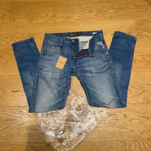 Replay Anbass jeans - Snygga blå slim fit jeans från Replay med klassisk femficksdesign och diskreta slitningar framtill. Jeansen har röda detaljer på insidan av linningen och är tillverkade i denim med lätt stretch för extra komfort.