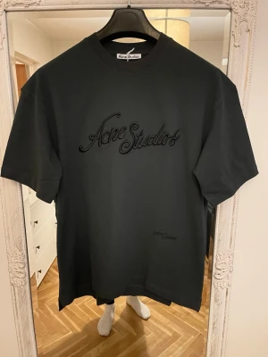 Svart Acne Studios t-shirt - Säljer en svart t-shirt från Acne Studios med broderad logga framtill i matchande svart ton. Klassisk rund hals och korta ärmar. Perfekt basplagg med stilren design och exklusiv känsla.