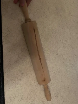 Trä kavel med handtag - En klassisk kavel i trä med två handtag, perfekt för att kavla ut deg till bakning. Kaveln har en naturlig träfärg och en avlång, cylindrisk form. Passar bra i köket för dig som gillar att baka bröd, kakor eller pizza.