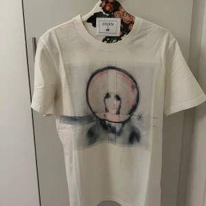 Vit t-shirt med konstnärligt tryck från gvc  - Vit t-shirt från givenchy med ett konstnärligt tryck av ett ansikte i svart, rosa och grå toner på framsidan. Klassisk rund halsringning och korta ärmar. Perfekt för dig som gillar unika plagg med cool design. Storlek Large