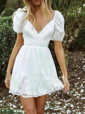 Vit spetsklänning med puffärm - Super populär klänning! Kort vit klänning med v-ringning, puffärmar och fina spetsdetaljer längs urringning och fåll. Klänningen har en omlottliknande överdel och är tillverkad i ett lätt material som passar perfekt till varma dagar.