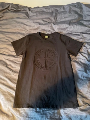 Svart Stone Island t-shirt i bomull - Säljer en svart t-shirt från Stone Island med det klassiska kompassloggan i relief på bröstet. T-shirten har rund hals och korta ärmar. Storlek S men sitter som en XS.