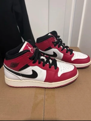 Air Jordan 1 Mid Chicago röd/vit - Säljer ett par Air Jordan 1 Mid Chicago med klassisk färgkombination i rött, vitt och svart. Skorna har svart swoosh, svarta skosnören och perforerad tåbox. Tillverkade i läder med ikoniska Jordan-loggor på sidan och plös. Perfekta för dig som gillar streetwear och sneakerskultur.
