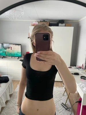 Svart croppad topp från H&M Divided - Säljer en svart, croppad topp från H&M Divided med rundad halsringning och korta ärmar. Perfekt för dig som gillar en slim och enkel stil. Materialet är mjukt och stretchigt, vilket gör den bekväm att bära hela dagen.