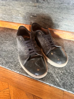 Lanvins  - Snygga svarta sneakers med mockaliknande material på sidorna och glansig lackdetalj på tån. Skorna har svarta snören och vit sula för en klassisk look. Perfekta för dig som gillar stilrena och moderna skor.