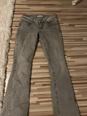 Grå bootcut jeans - Snygga grå jeans med bootcut-modell och klassiska fickor. Jeansen har detaljerade sömmar och knappar på bakfickorna. Perfekta för dig som gillar en avslappnad men ändå stilren look.