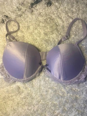 Vintage Y2K shimmer BH - Lilac / Lila ca 70C - Superfin, lila bh i metallic / Shimmer- tyg med vackra detaljer  Detaljer : rosett och ” diamant” i mitten. Axelband i spets med diskret glitter. Passform: hög triangelformad kupa (ca 15 cm hög) med jämnt lätt vaddering / Push- up.  Storlek: kladdlapp saknas men underbandet mäter 66 cm osträckt (motsvarar storlek 70) kupan uppskattas till C.  Skick: vintage, men i nyskick inga tecken på användning. Resåren är spänstig. 