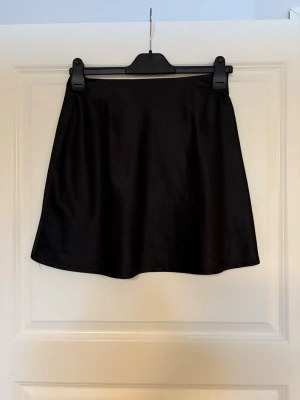 Svart satin kortkjol - Snygg svart kortkjol i satinliknande material. Lätt utställd form. Storlek M från chiquelle och i mycket bra skick🤗