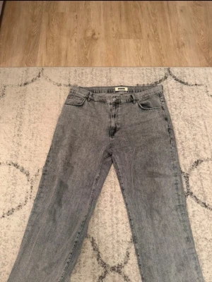 Grå jeans från Woodbird - Säljer ett par snygga grå jeans från Woodbird i klassisk rak modell. Jeansen har fem fickor, bälteshällor och knappgylf. Materialet är denim i tvättad grå nyans som ger en cool vintagekänsla. Perfekta för en avslappnad och trendig stil.