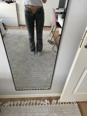 Grå raka jeans med hög midja - Säljer ett par grå jeans med rak passform och hög midja. Jeansen har klassisk femficksdesign och knappgylf. Perfekta för en avslappnad och trendig look. Materialet är denim i bomull. Passar dig som gillar en enkel men snygg stil.
