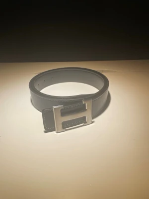 Blå skärp med silverfärgat H-spänne - Snyggt svart bälte i skinn med ett stort, silverfärgat H-format spänne. Perfekt accessoar för att lyfta vilken outfit som helst. Klassisk design med stilrena sömmar och justerbar längd.