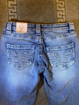 Blå bootcut jeans XS från Gina tricot - Säljer ett par blå bootcut jeans från Gina tricot i storlek XS. Jeansen har låg midja, utsvängda ben och snygga detaljerade bakfickor med kontrastsömmar. Perfekta för dig som gillar retrostil och vill ha ett par riktigt low waist jeans! 