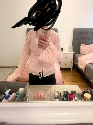 Ljusrosa spetsig bolerotopp med knyt - Superfin ljusrosa bolerotopp i spets med långa utsvängda ärmar och knyt framtill. Tunt och luftigt material med romantisk känsla, perfekt att styla över ett linne eller klänning. Söt volangkant längs nederdelen och ärmsluten.