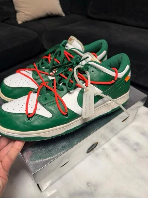 Nike Off-White Dunk Low Grön/Vit - (ÄKTA KÖPTE FÖR 8,2)Nike Off-White Dunk Low sneakers i grön och vit färg med röda detaljer. Skorna har dubbla snörningar, Off-White text på sidan och klassisk Nike-logga på hälen. Materialet är läder och textil, och designen är riktigt unik och trendig.